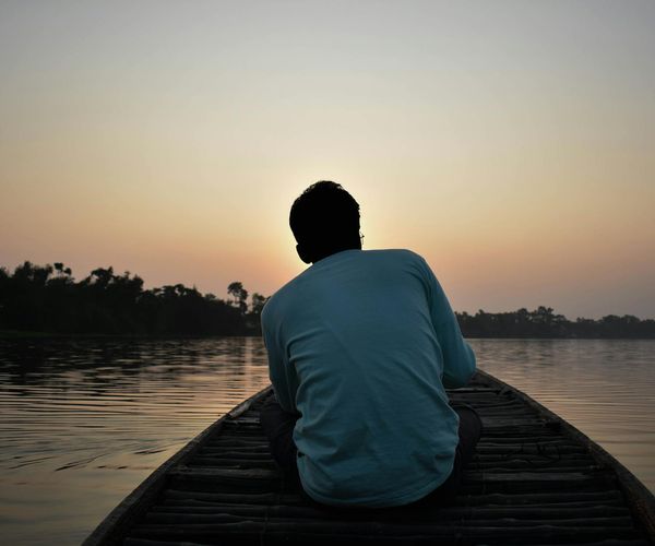 Peaceful person sitting in meditation by the water at sunrise.
